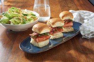 Photo of 3 grilled salmon sliders on a table with a side salad
